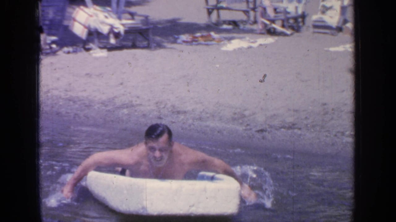 Man paddling a small white boat with his hands in lake water.