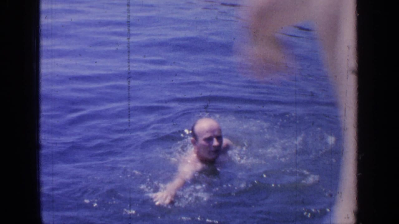 Adult man swims in the blue water at Greenwood Lake in a 1964 8mm home-movie frame.