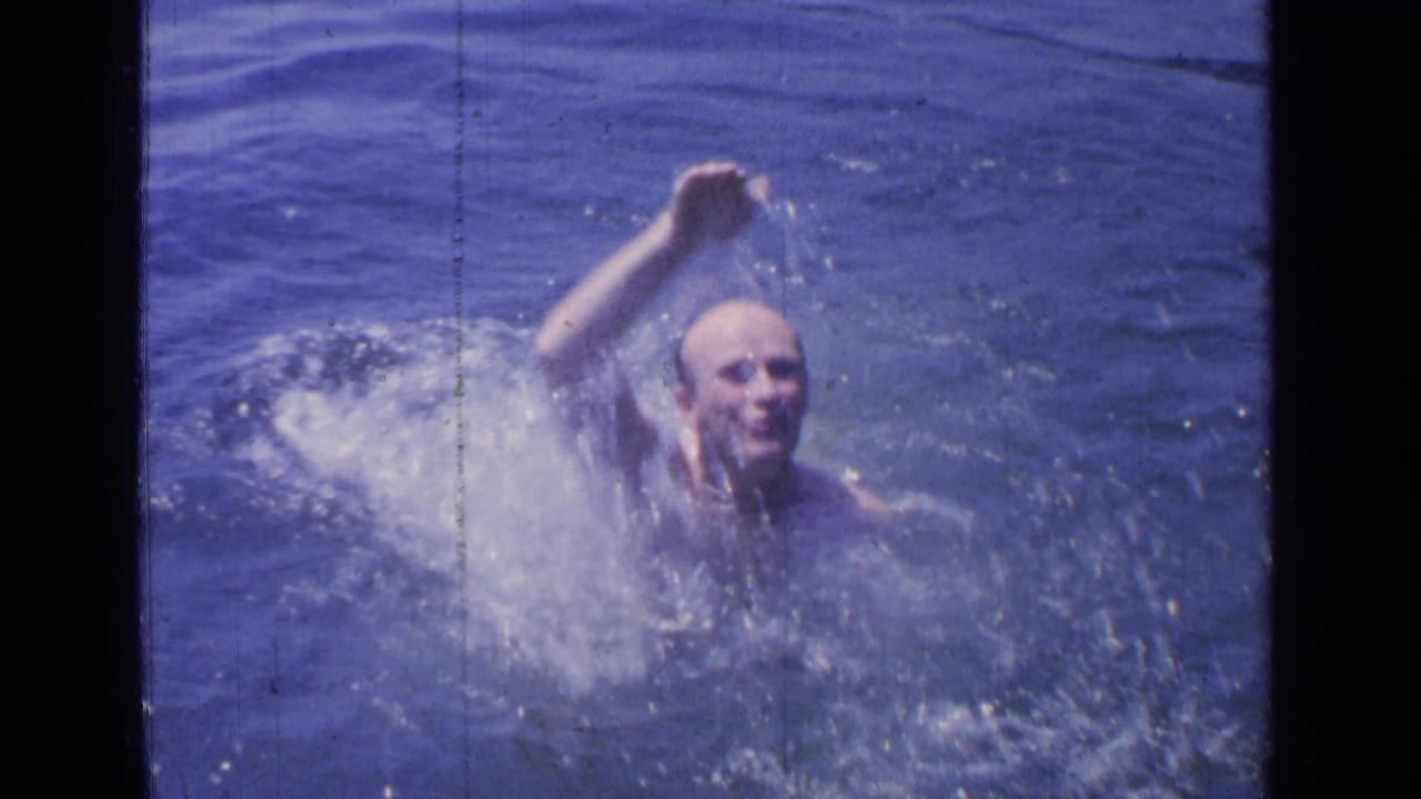 The swimmer appears above the water at Greenwood Lake, smiling or grimacing with effort as one arm lifts through spray.