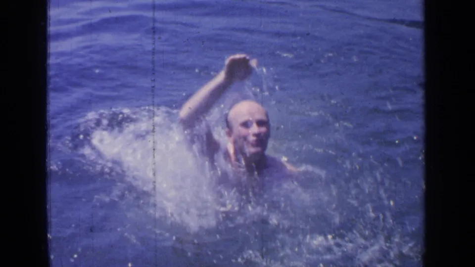 The swimmer appears above the water at Greenwood Lake, smiling or grimacing with effort as one arm lifts through spray.