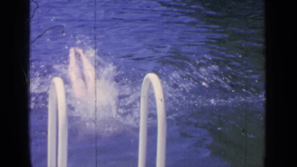 White ladder rails frame the foreground while the swimmer passes behind them in the Greenwood Lake swimming area.