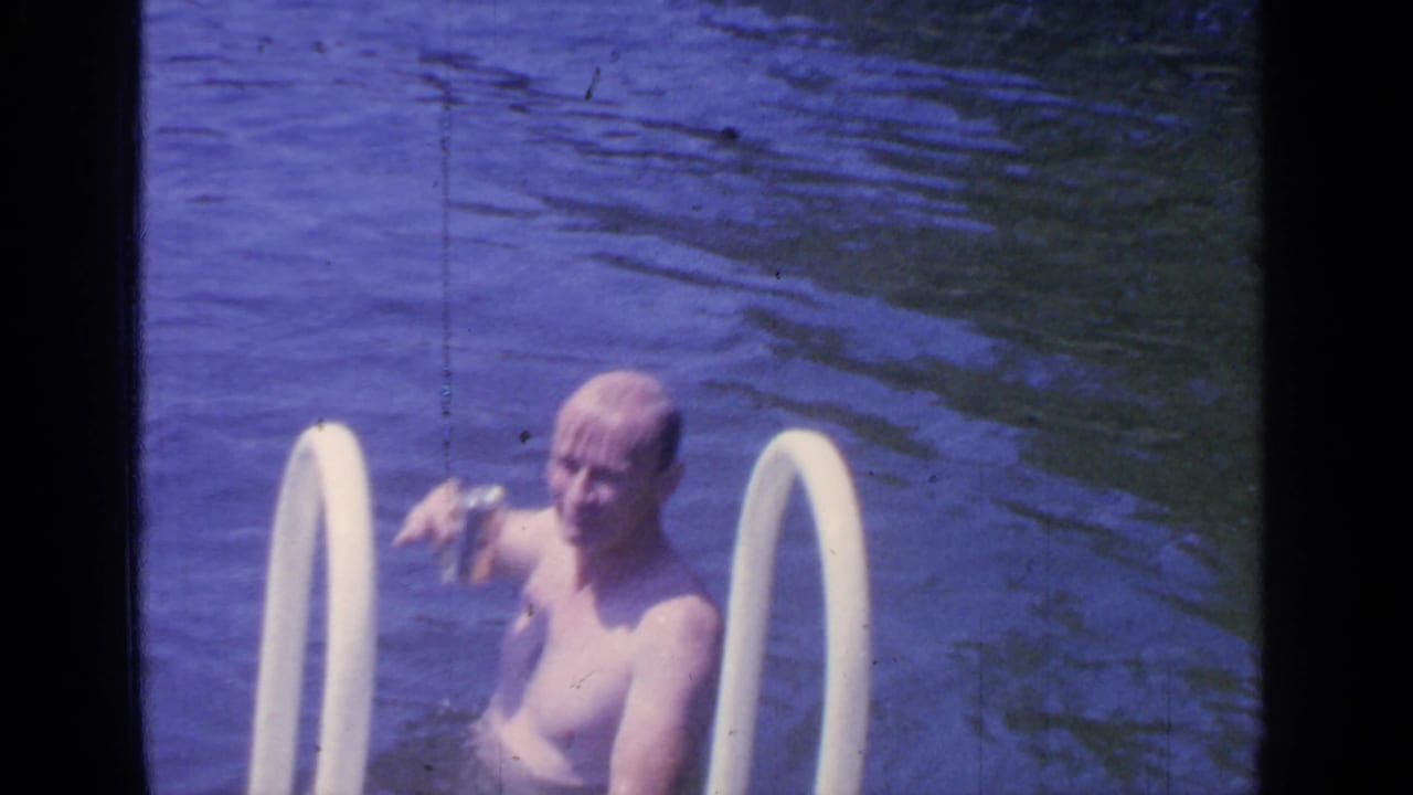 The man lowers the can while standing in Greenwood Lake water near the white ladder, with his face visible toward the camera.