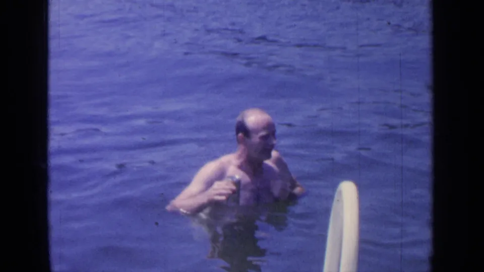 The man appears to gesture or speak while standing in Greenwood Lake water, with the white ladder at the right edge of the frame.