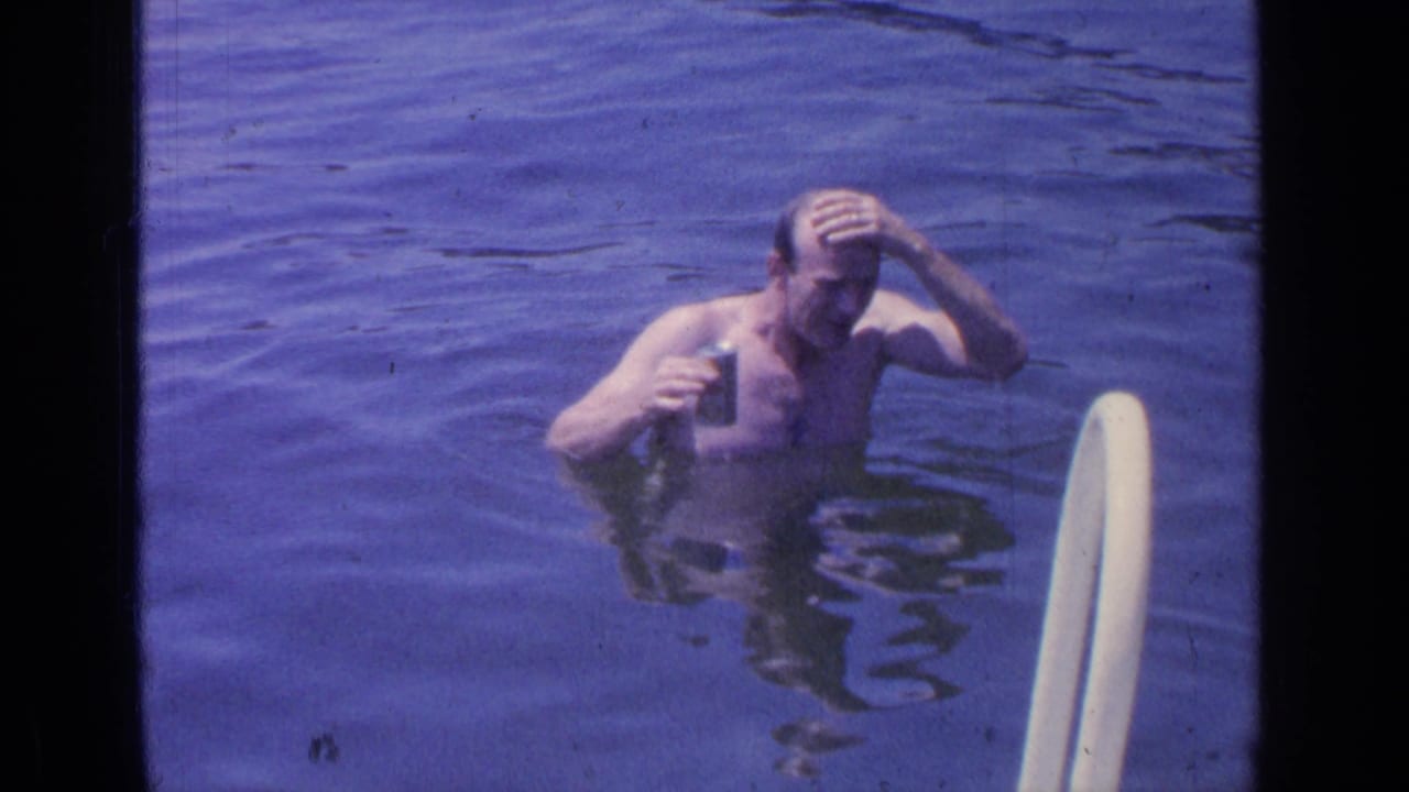 Man in lake water touches his head while holding a can near a white ladder.