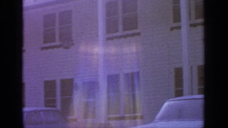 The final 1964 Greenwood Lake frame shows a faded building exterior, windows, and part of a parked car under strong color shift.