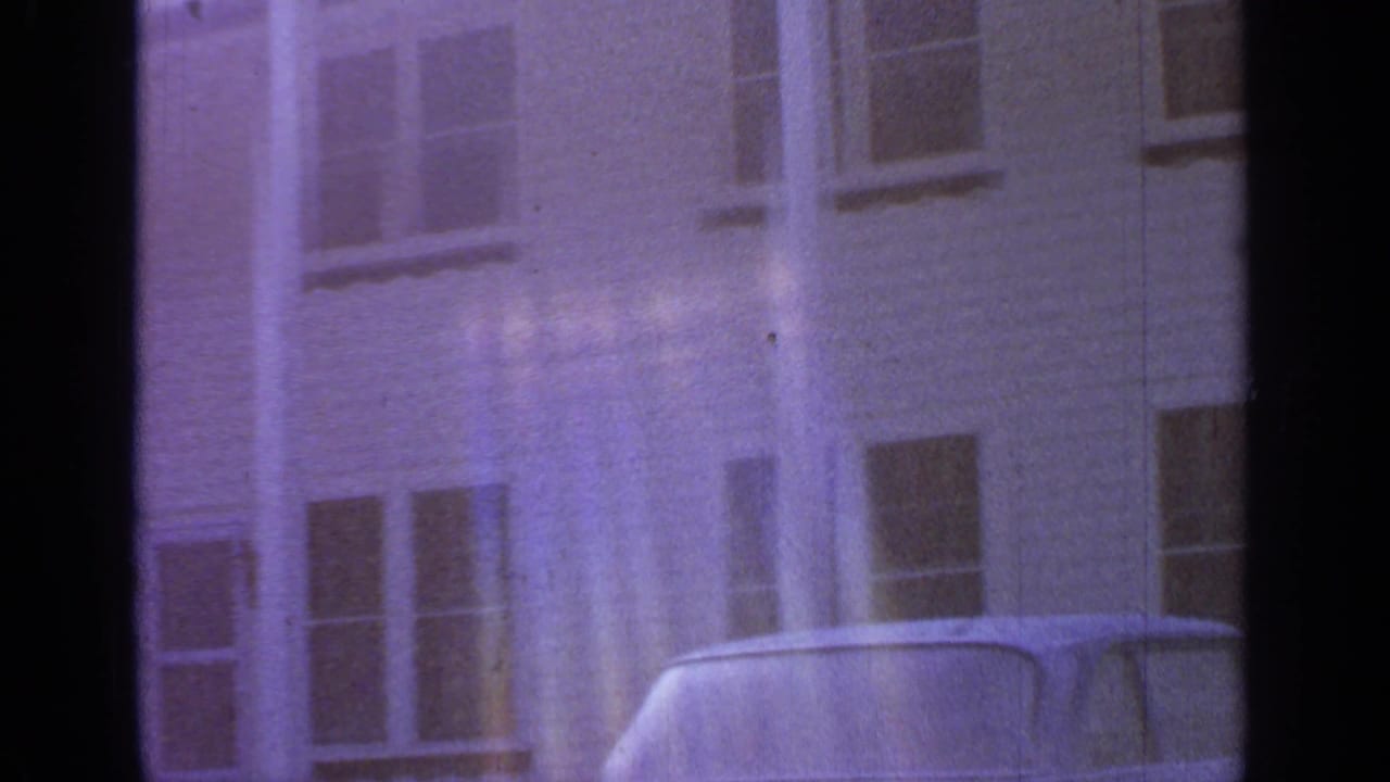 White clapboard house exterior with windows, a partial car, and vertical light flares.