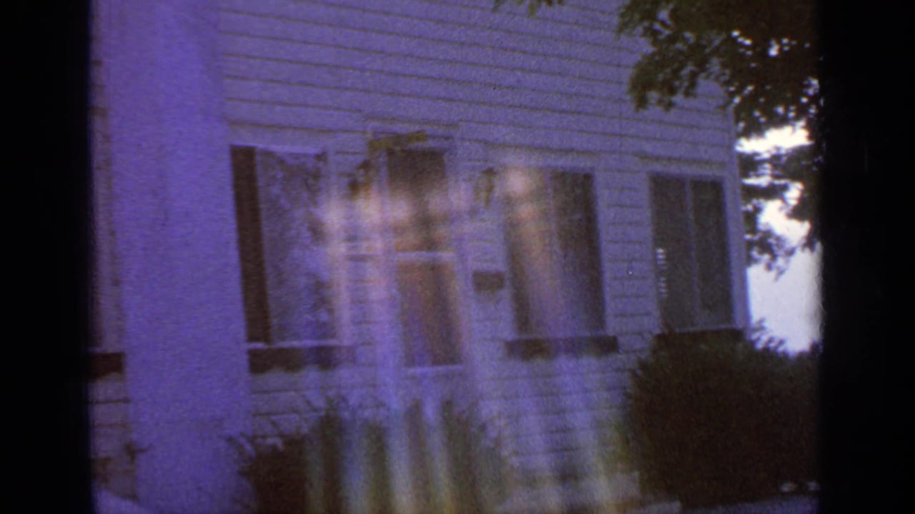 Greenwood Lake house exterior with clapboard siding, shuttered windows, bushes, tree edge, and strong 8mm flare streaks.