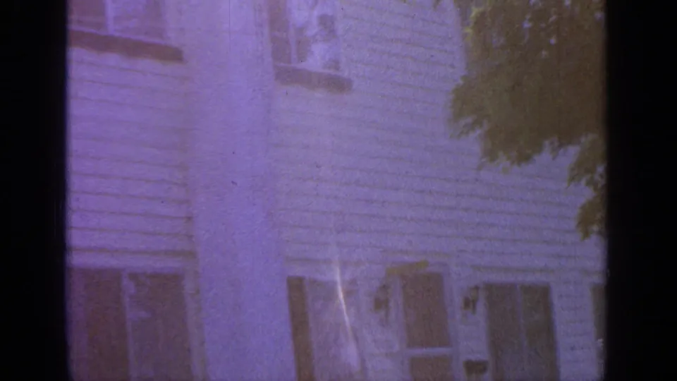 Greenwood Lake 1964 frame of a clapboard house side with windows, tree foliage, purple color shift, and visible film gate edge.