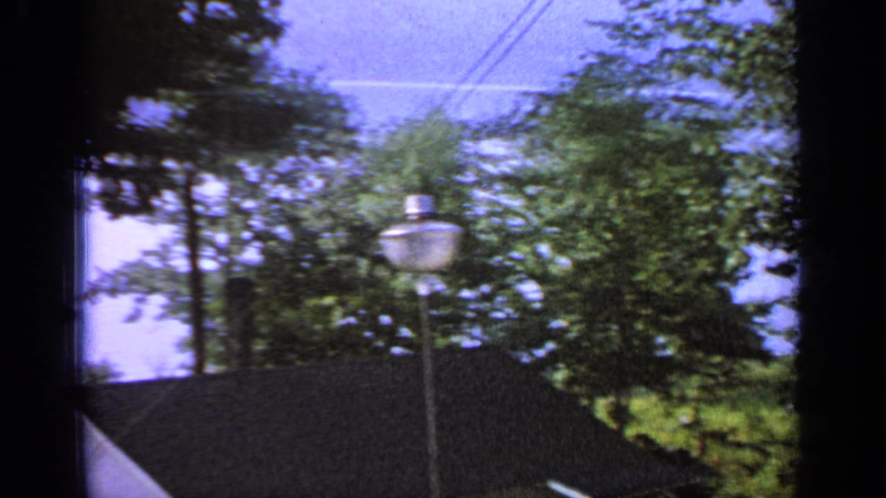 1964 Greenwood Lake home-movie frame showing a street lamp, tree canopy, utility wires, and part of a house roof.