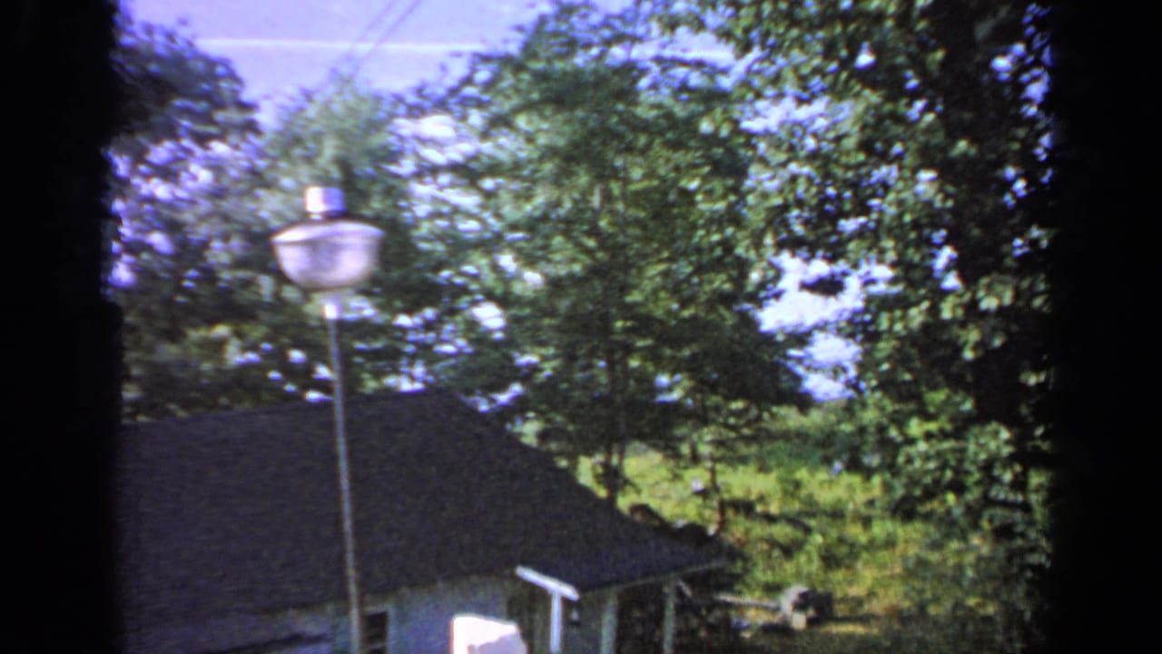 1964 Greenwood Lake frame with a lamp post in front of leafy trees and a dark-roofed residential building.