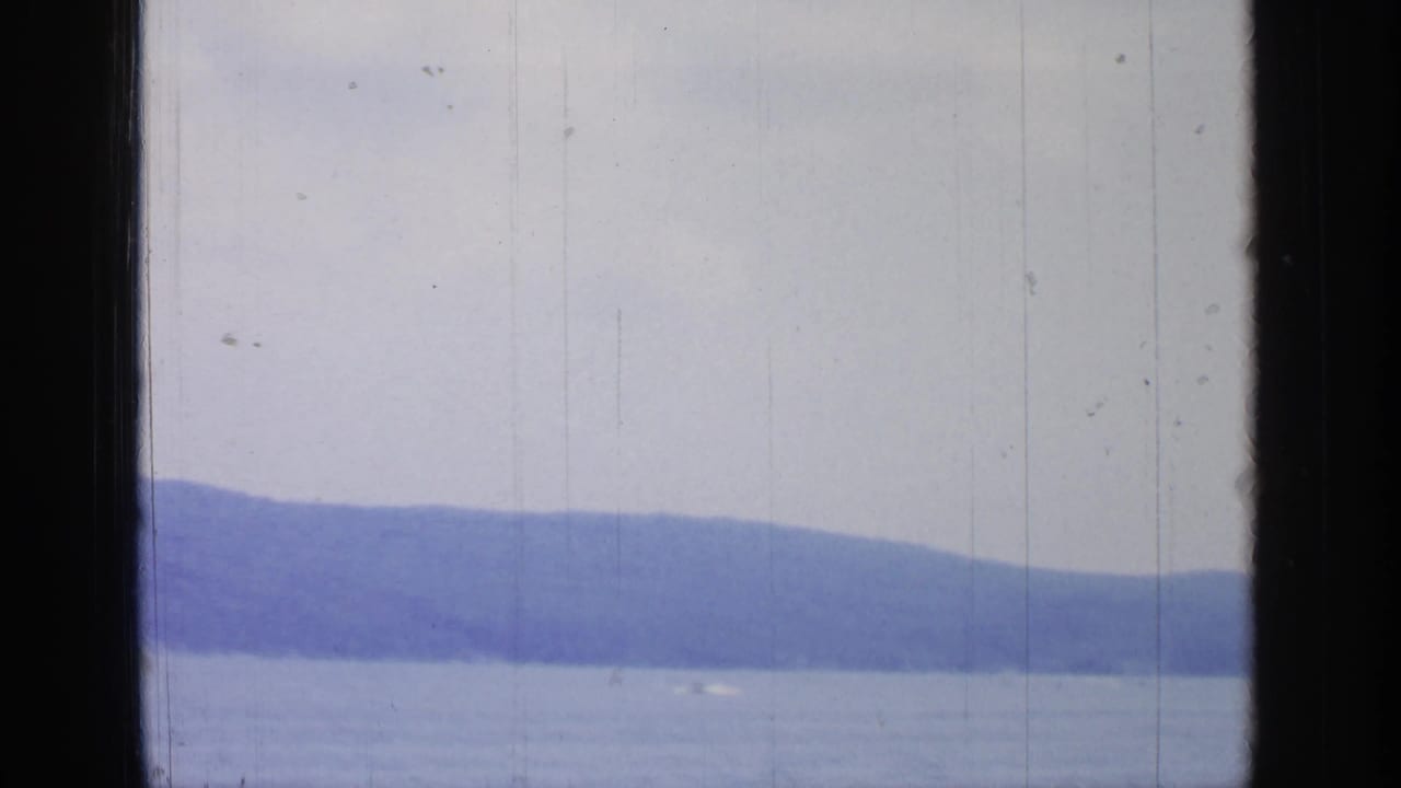 Greenwood Lake, New York, appears across the frame with a wooded hillside, open water, pale sky, and visible 8mm film wear.