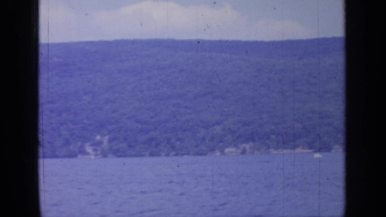 Blue lake water with a wooded hillside beyond, seen between dark vertical frame edges.