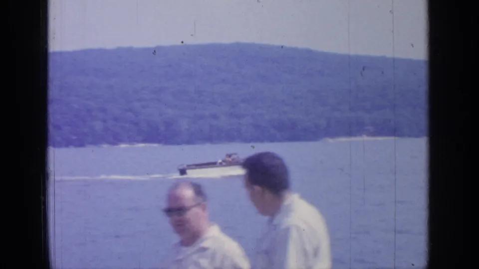 Greenwood Lake motorboat scene with two adult men in the foreground and wooded hills across the water, shot on 8mm in 1964.