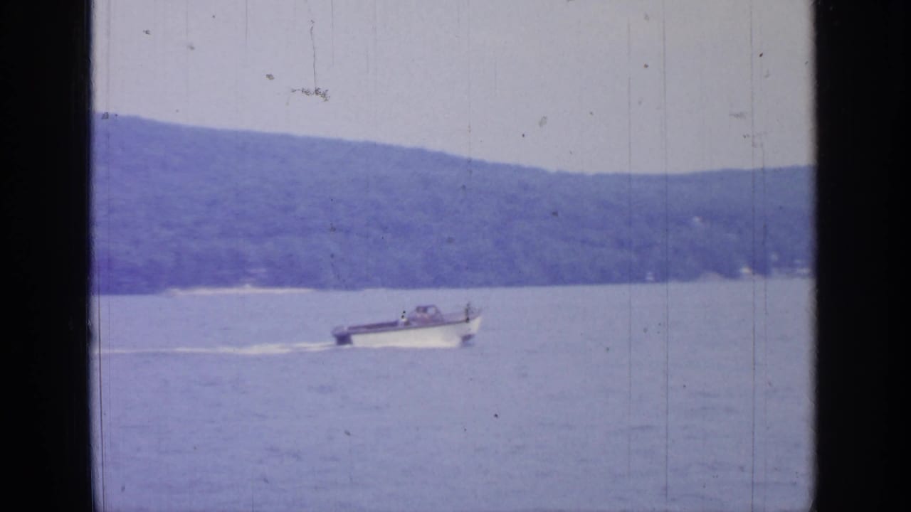 Speedboat crosses calm lake water with wooded hills in the background.