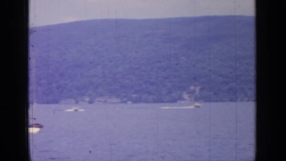 1964 Greenwood Lake frame showing a partial sailboat at the edge, open water, and small boats by a wooded shore.
