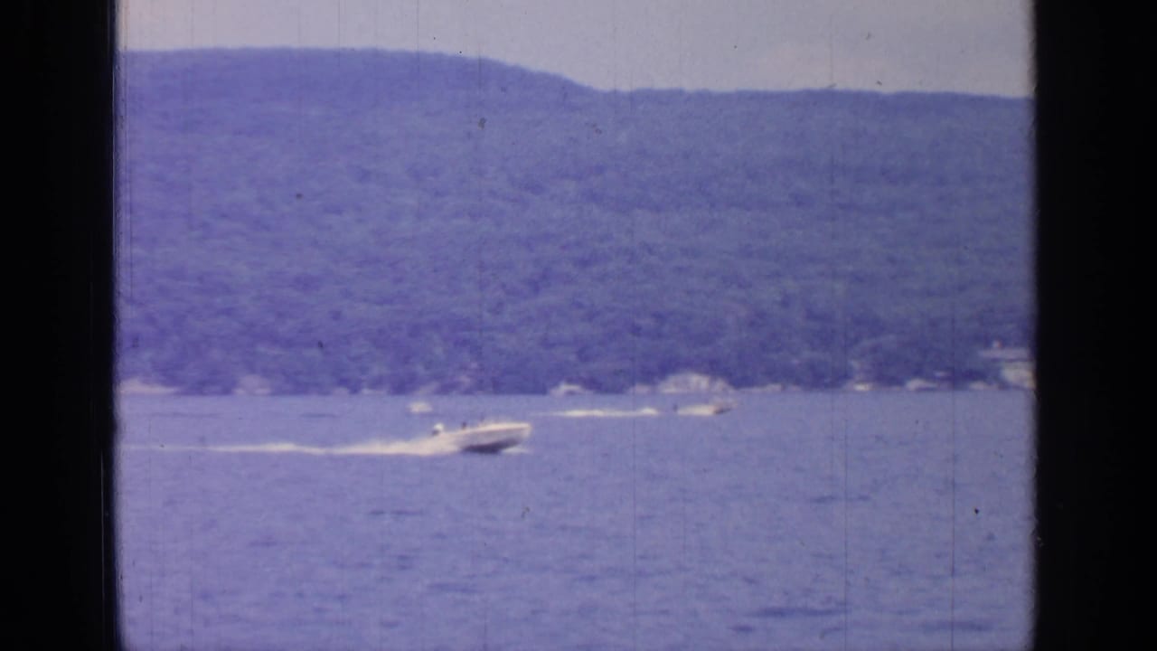 1964 Greenwood Lake frame with a speedboat moving across open water near a wooded shoreline.