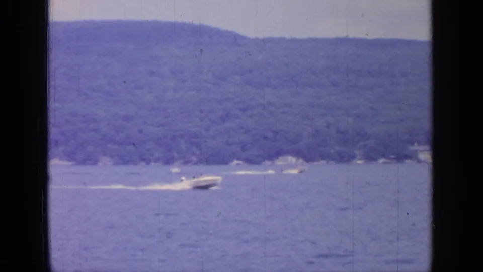 1964 Greenwood Lake frame with a speedboat moving across open water near a wooded shoreline.