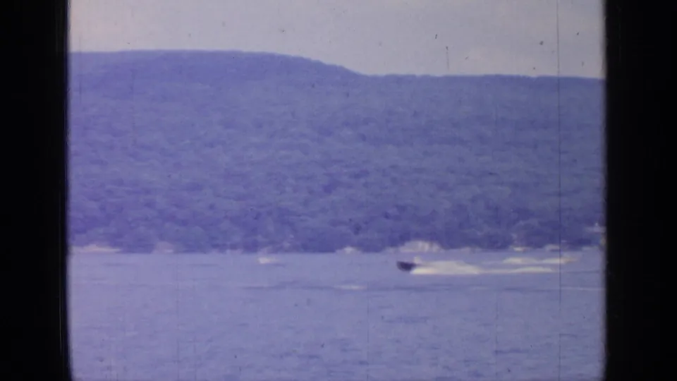 1964 Greenwood Lake frame showing a small speedboat and wake against a wooded lakeside backdrop.