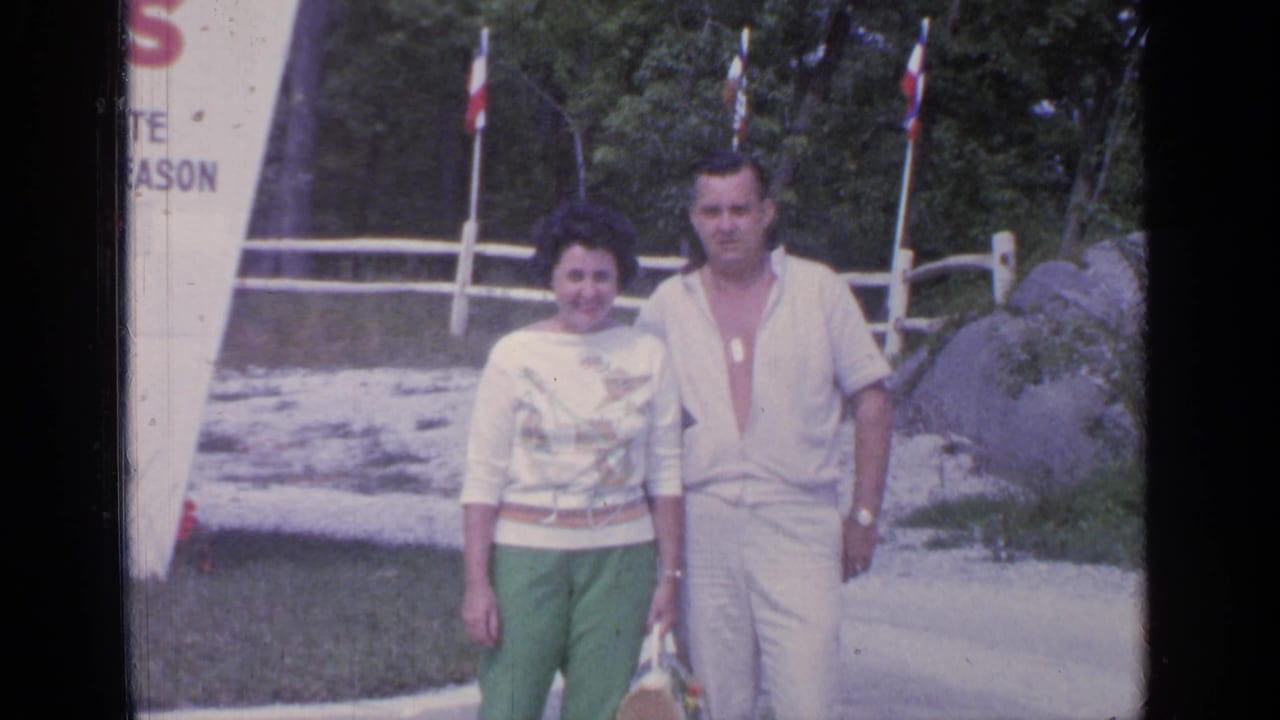 Smiling adult couple walking outdoors beside a partial white sign and fence.