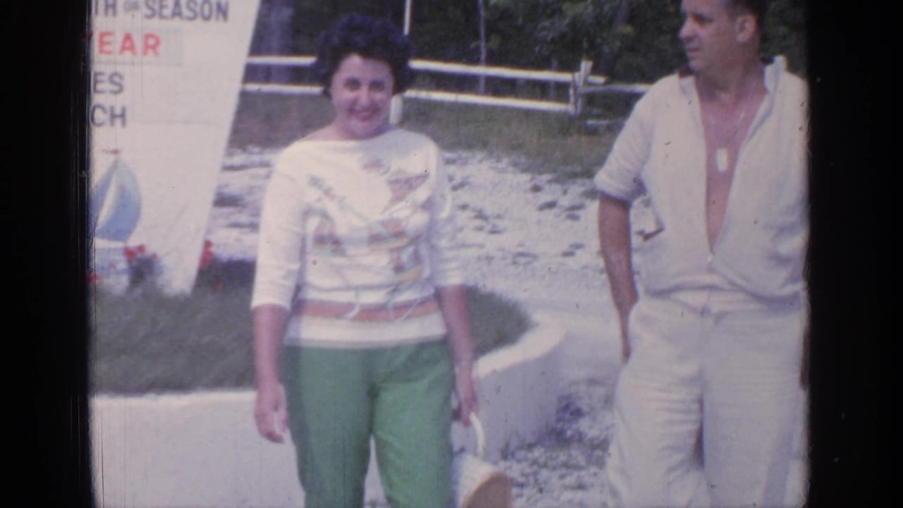 Couple walking near a seasonal beach sign in a sunny resort area.