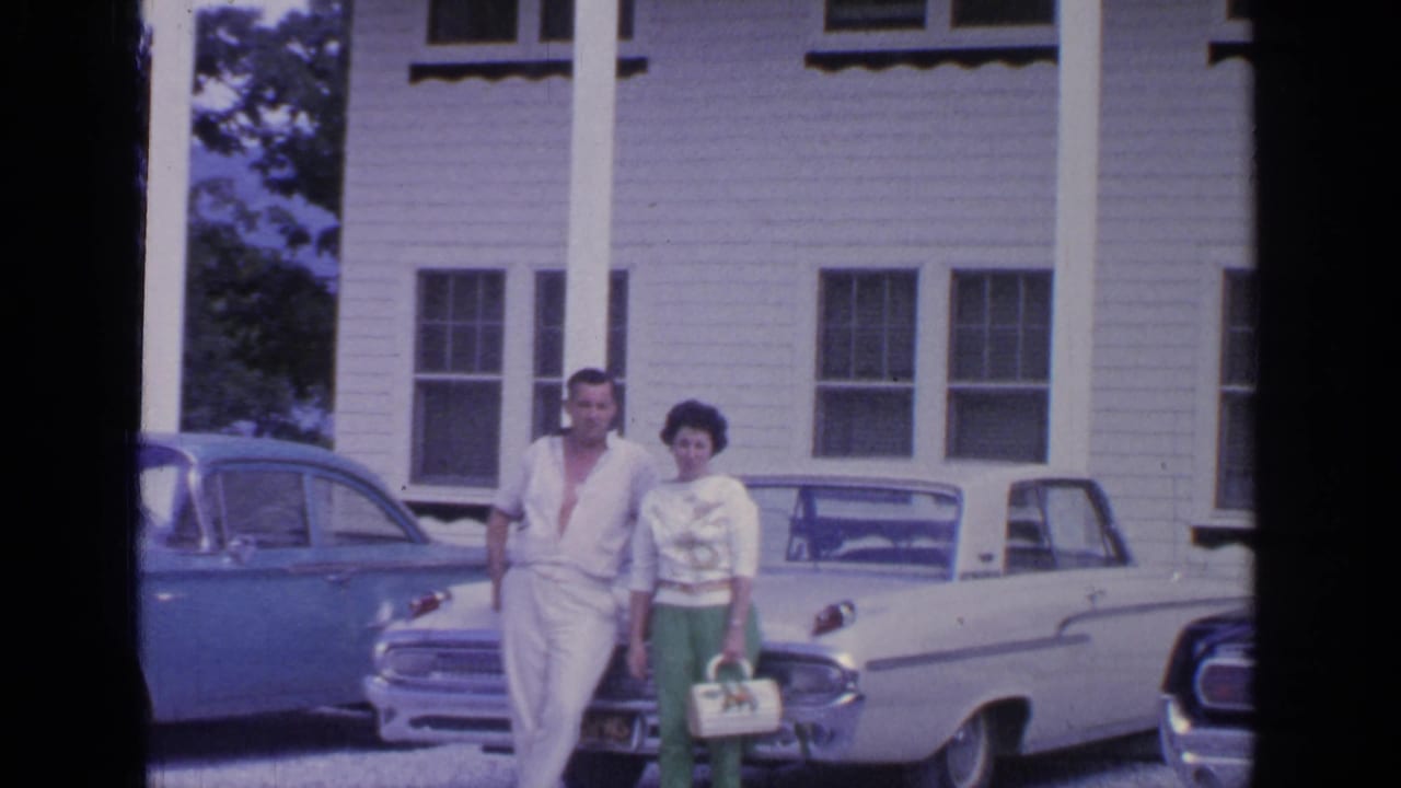 The couple remains posed in front of the house, with the white convertible and blue sedan framing the 1964 Greenwood Lake scene.