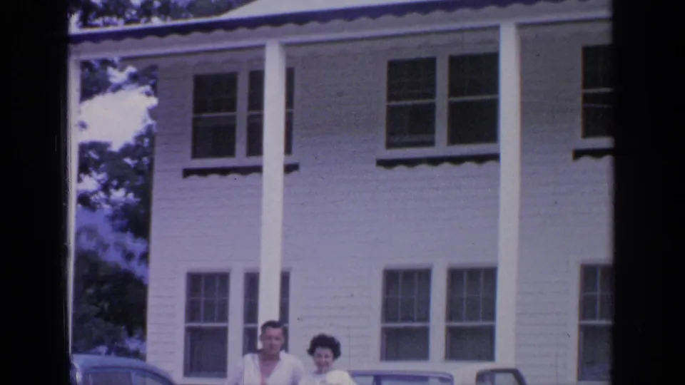 The final frame crops the couple low in the scene beneath the house windows, with the white convertible still visible beside them.