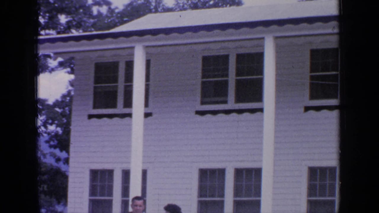 Two-story white clapboard house with columns, windows, and two partial adults near the lower edge.