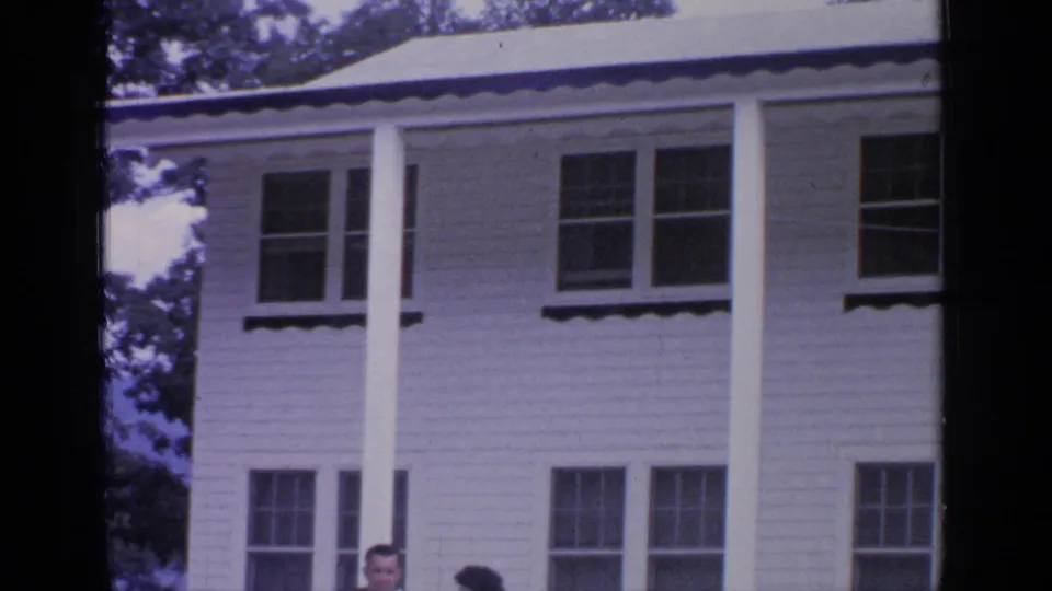 Greenwood Lake, New York home-movie frame showing a white two-story house with porch columns and partial adult figures at the bottom.
