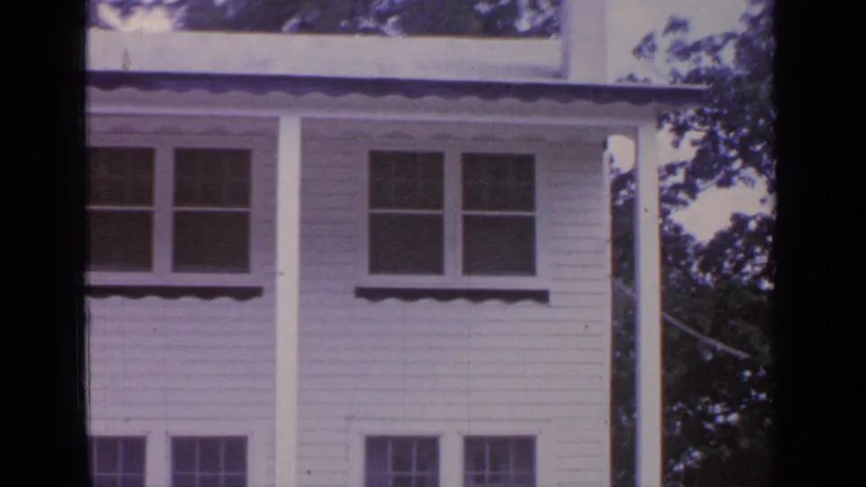 1964 Greenwood Lake home-movie view of the house exterior, showing windows, porch columns, and trees along one side.