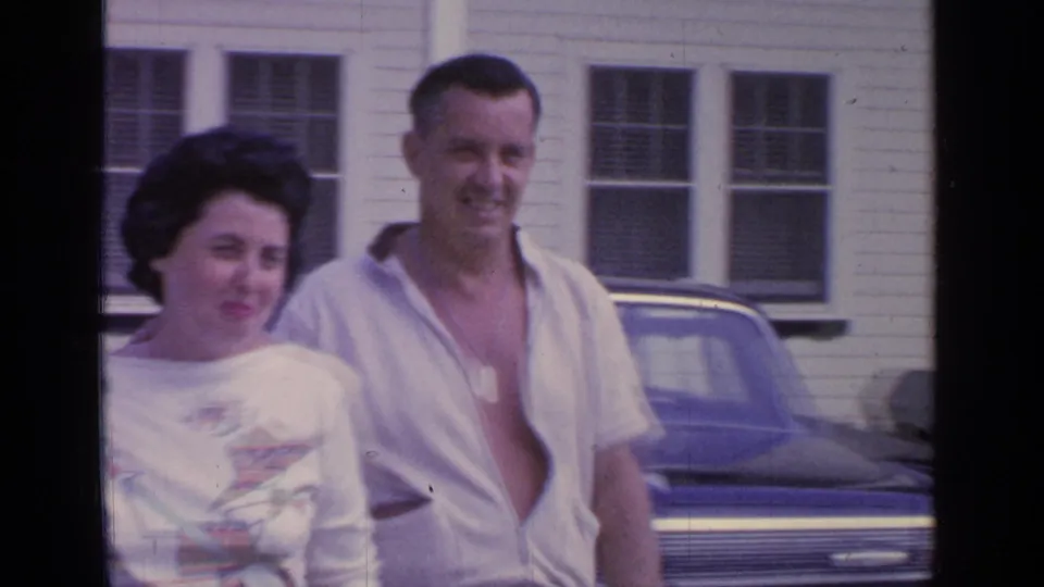A closer home-movie view shows the couple smiling near a parked car outside the Greenwood Lake building.