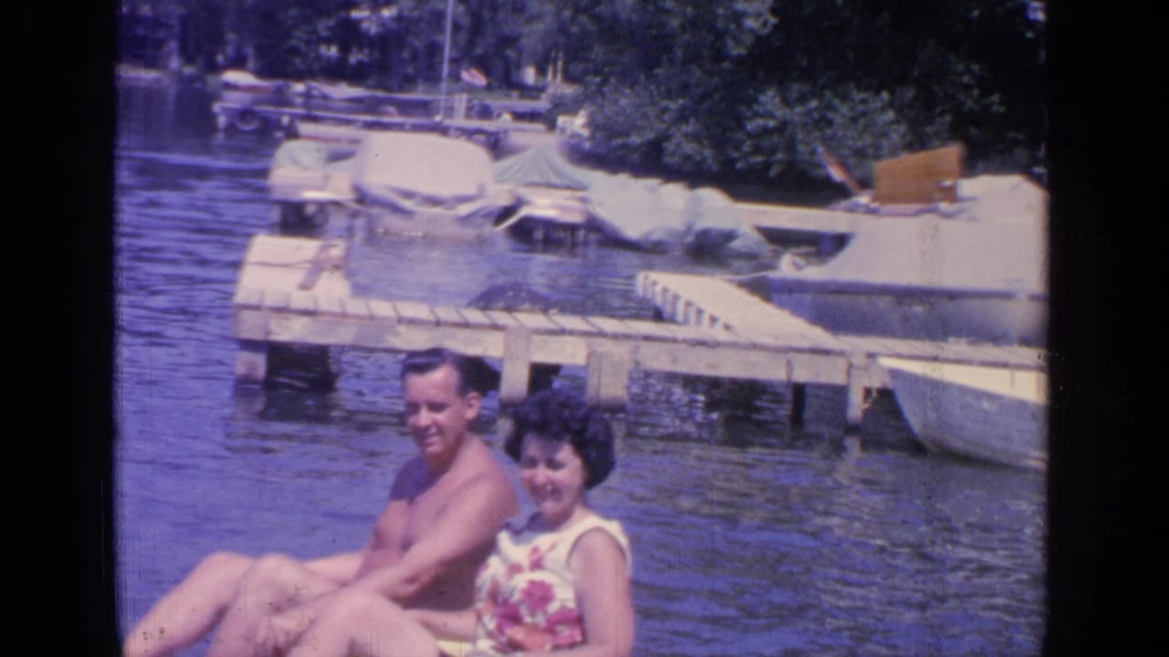 Man and woman sitting together on the water with docks and boats behind them.