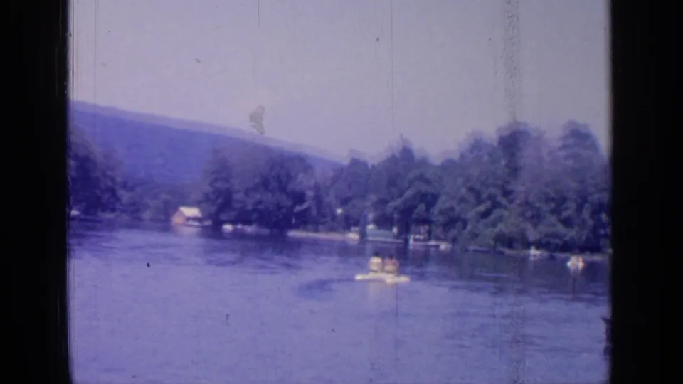 A wide 1964 Greenwood Lake view shows open water, wooded shoreline, low hills, and small recreational boats in the distance.