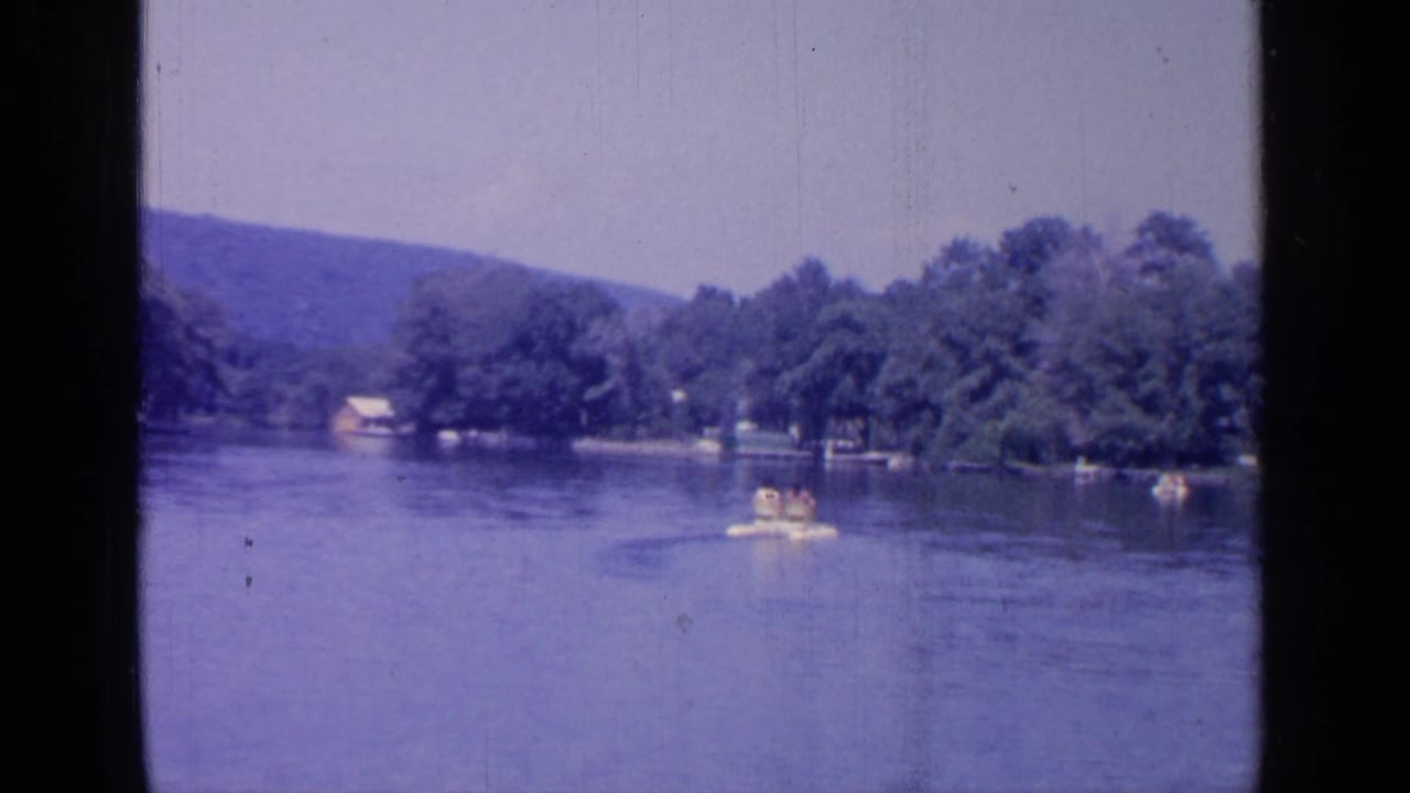 Small recreational boat crosses calm lake water near a wooded shoreline and distant hills.