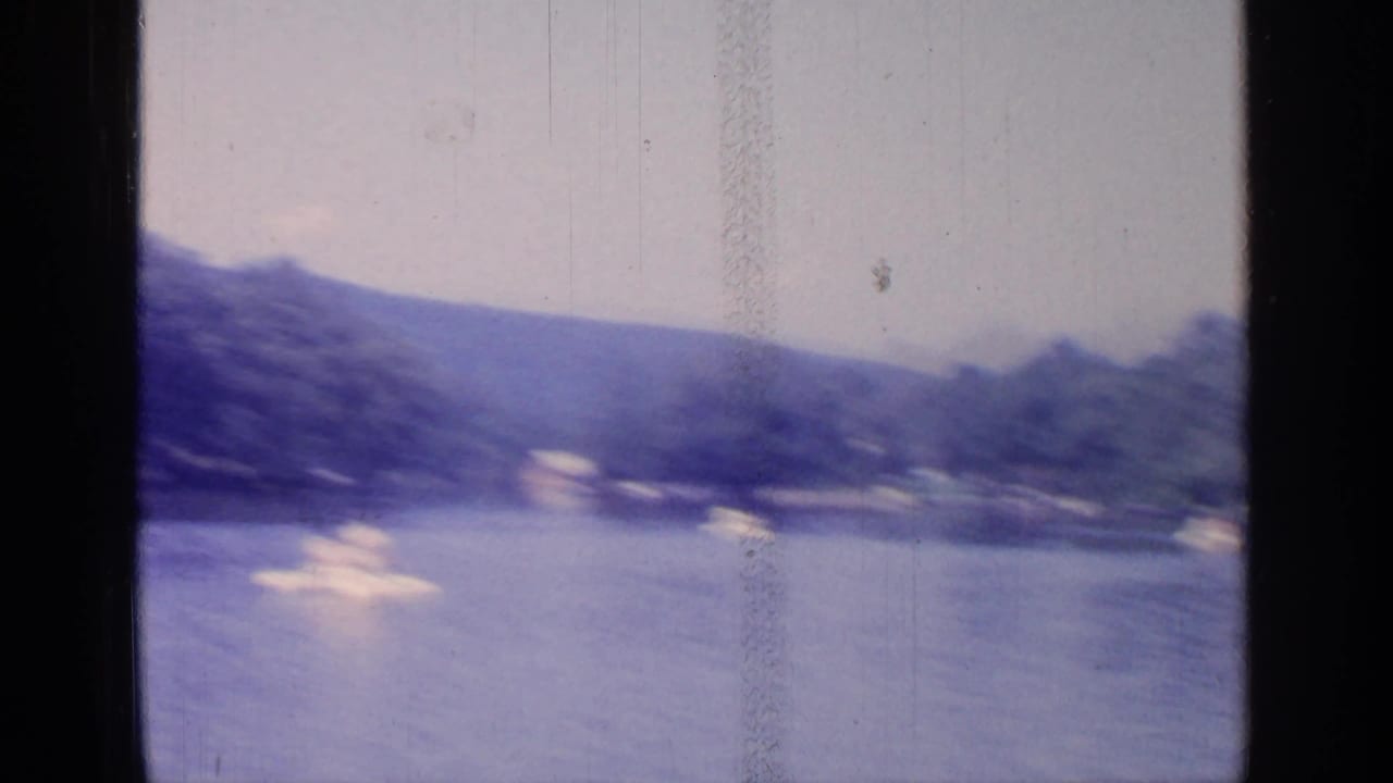 Soft, distant view of small boats on a lake below wooded hills.