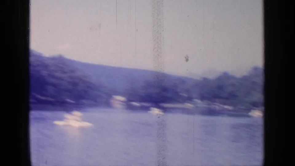 Soft 1964 Greenwood Lake frame with small paddleboats spread across the water and wooded hills in the distance.