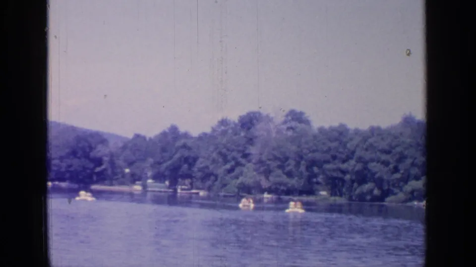 Wide Greenwood Lake view from 1964 showing several small boats on calm water against a dense tree-lined shore.