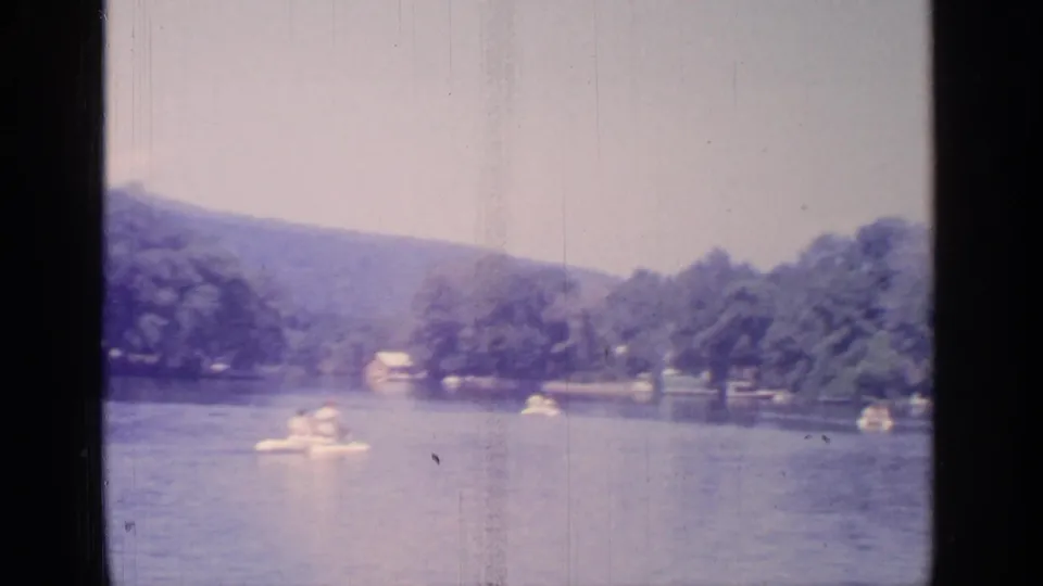 1964 Greenwood Lake frame showing a white paddleboat in the foreground and other small boats near the wooded shore.