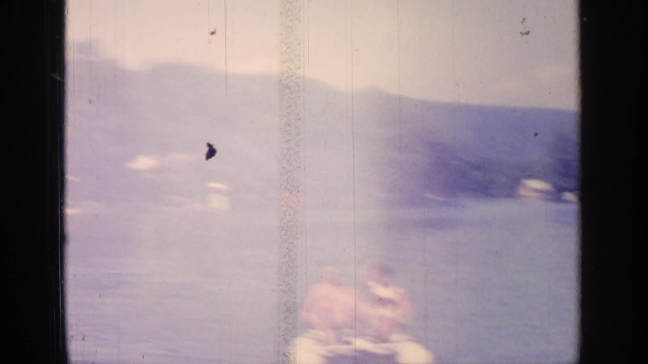 Faded frame of a paddle boat on a lake with wooded hills in the background.