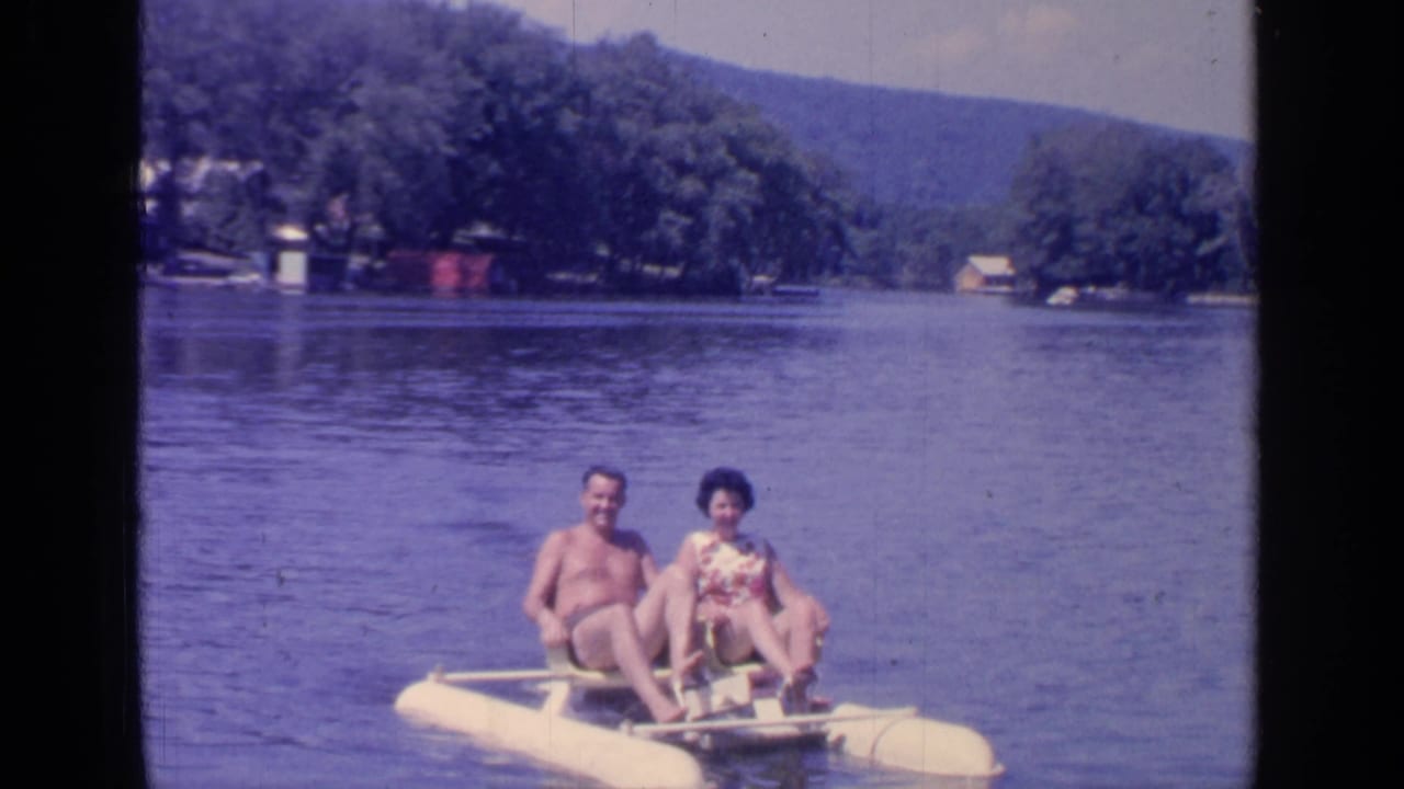 Couple seated on a yellow paddleboat on open lake water with wooded hills behind them.