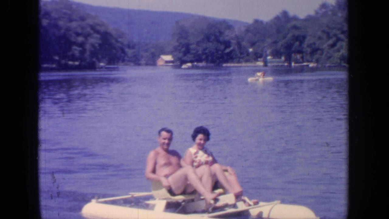 Couple seated on a small water wheeler on a lake with wooded hills behind them.