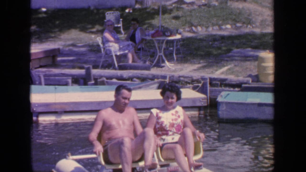 Adult couple seated in a yellow pedal boat near a dock on a lake.