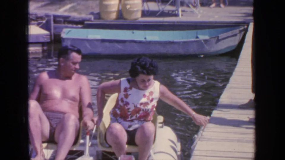 Greenwood Lake 1964 frame showing the couple alongside the dock in a yellow pedal boat with another boat behind them.