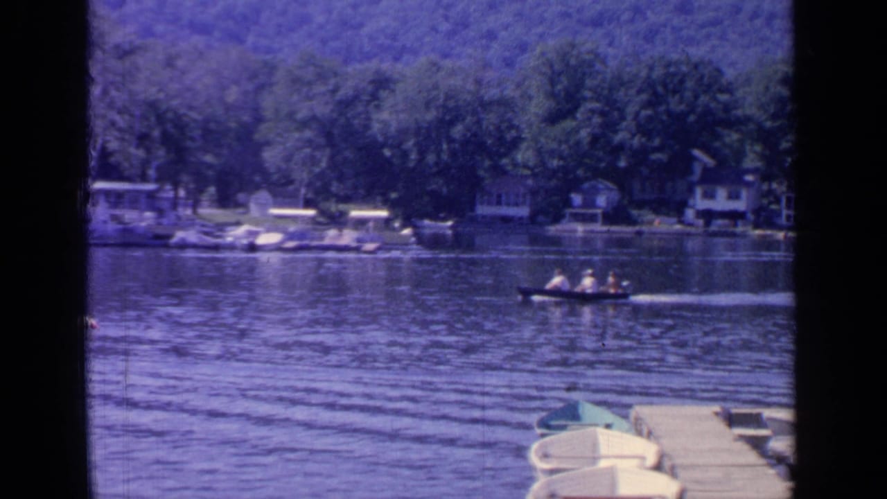 Small motorboat crossing a lake near cottages, with docked boats in the foreground.
