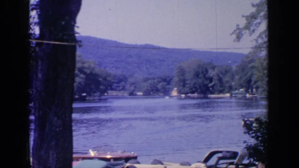 1964 Greenwood Lake home-movie frame looking down the water toward wooded shores, distant hills, and small boats near the lower edge.