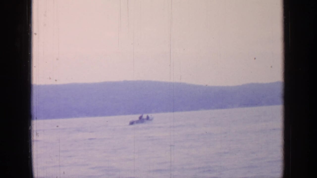 Small motorboat crosses a calm lake with wooded hills in the distance.