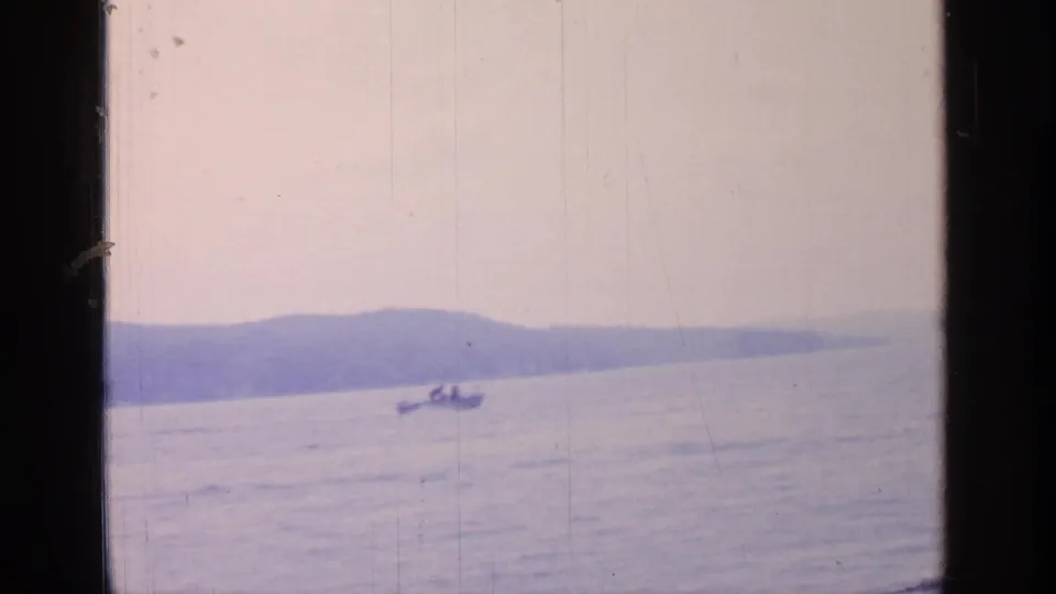 Final 1964 Greenwood Lake frame showing the small motorboat farther right, distant hills, calm blue water, and dark film-window framing.