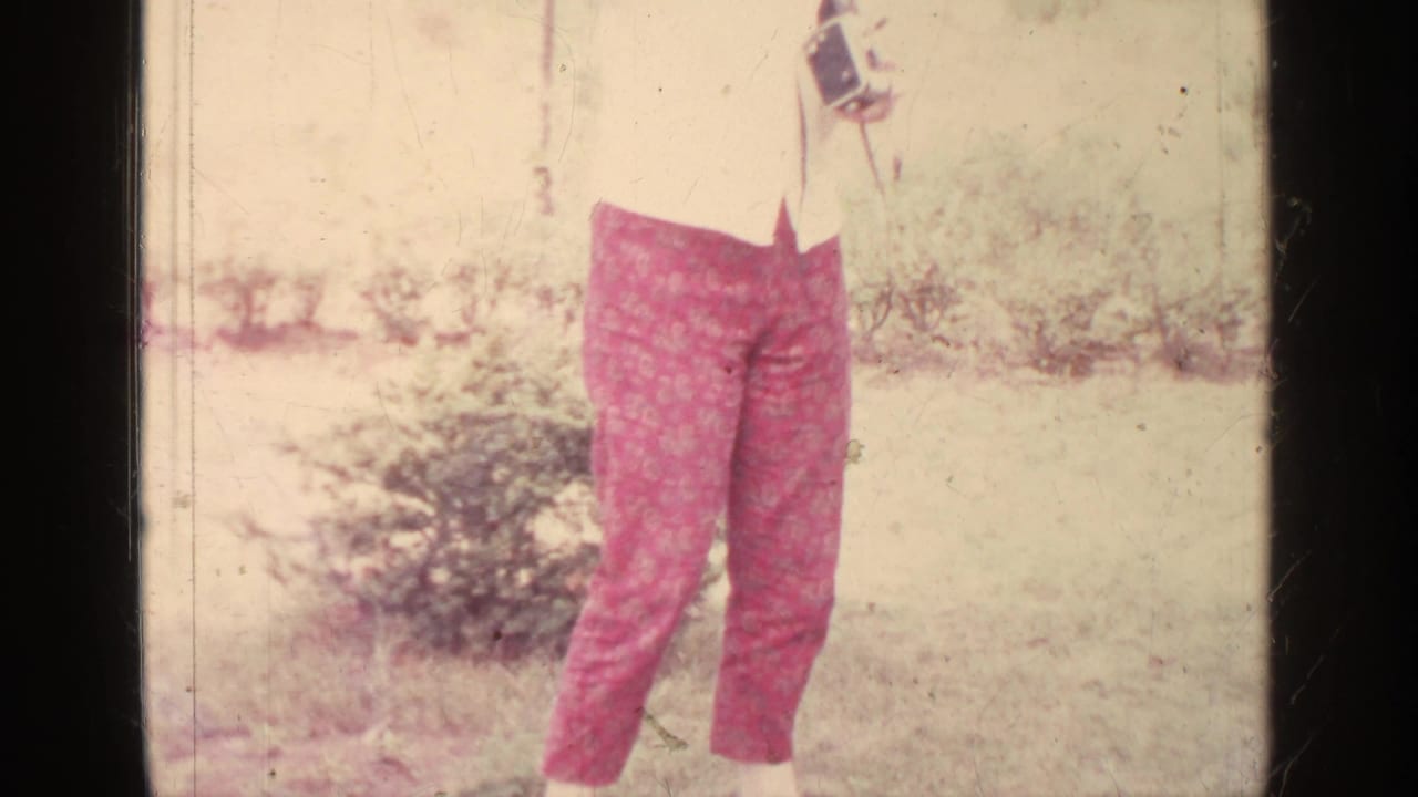 Cropped view of a woman holding a film camera, with red patterned pants visible.