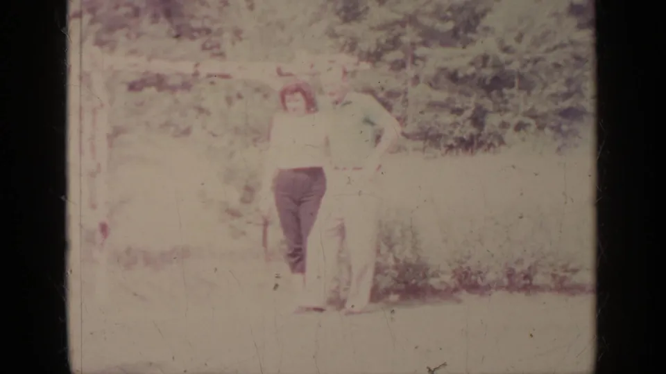 A distant adult man appears in the outdoor 1964 Greenwood Lake home-movie footage amid trees and grass.