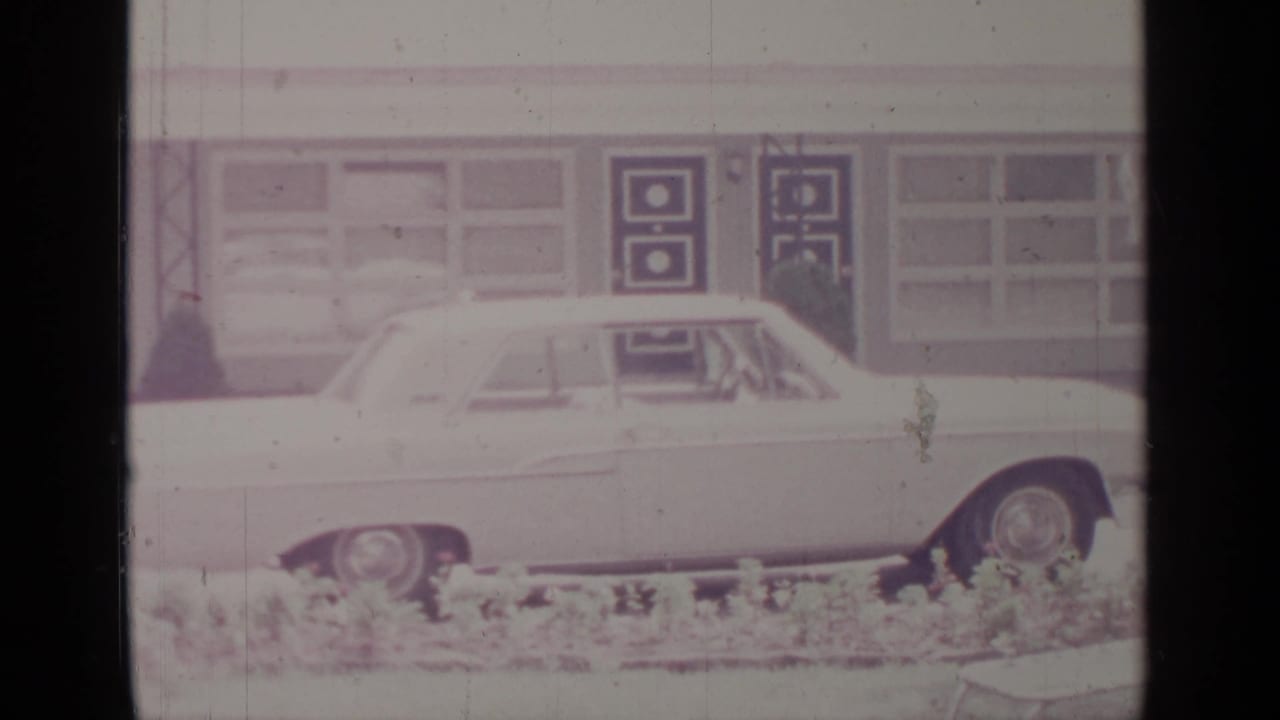 White car seen from the side in front of windows and dark geometric doors.