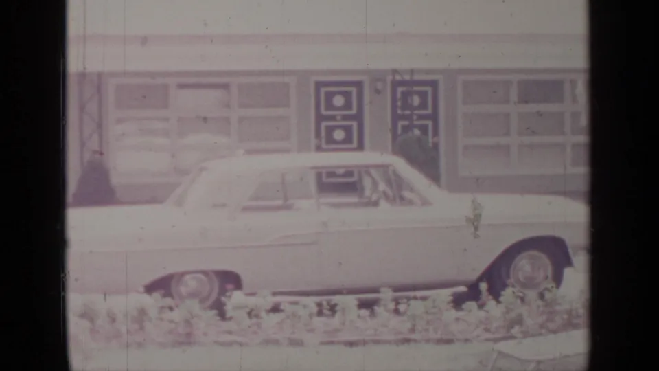Side view of a white sedan in Greenwood Lake, New York, with a mid-century facade and dark geometric door panels behind it.